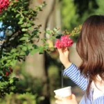 a young girl holding a cup of coffee and smelling flowers