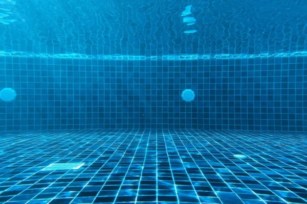 An underwater view of a blue tiled swimming pool with a drain